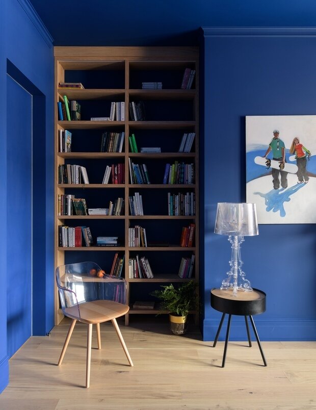 В спальне в нише поместился стеллаж с книгами. Его выделили цветом натурального дерева на фоне синих стен.