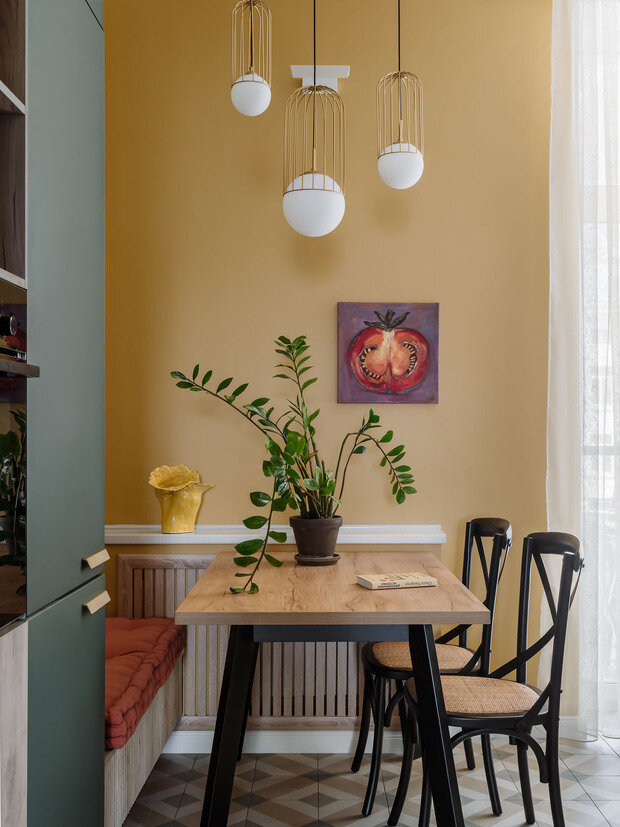 Одну из стен кухни выкрасили в яркий жизнерадостный желтый оттенок. В обеденной зоне предусмотрели несколько вариантов освещения: настенная подсветка и подвесные светильники. 